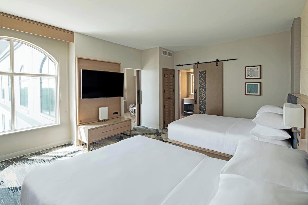 A hotel room with two beds, a TV, a desk, and a large window.