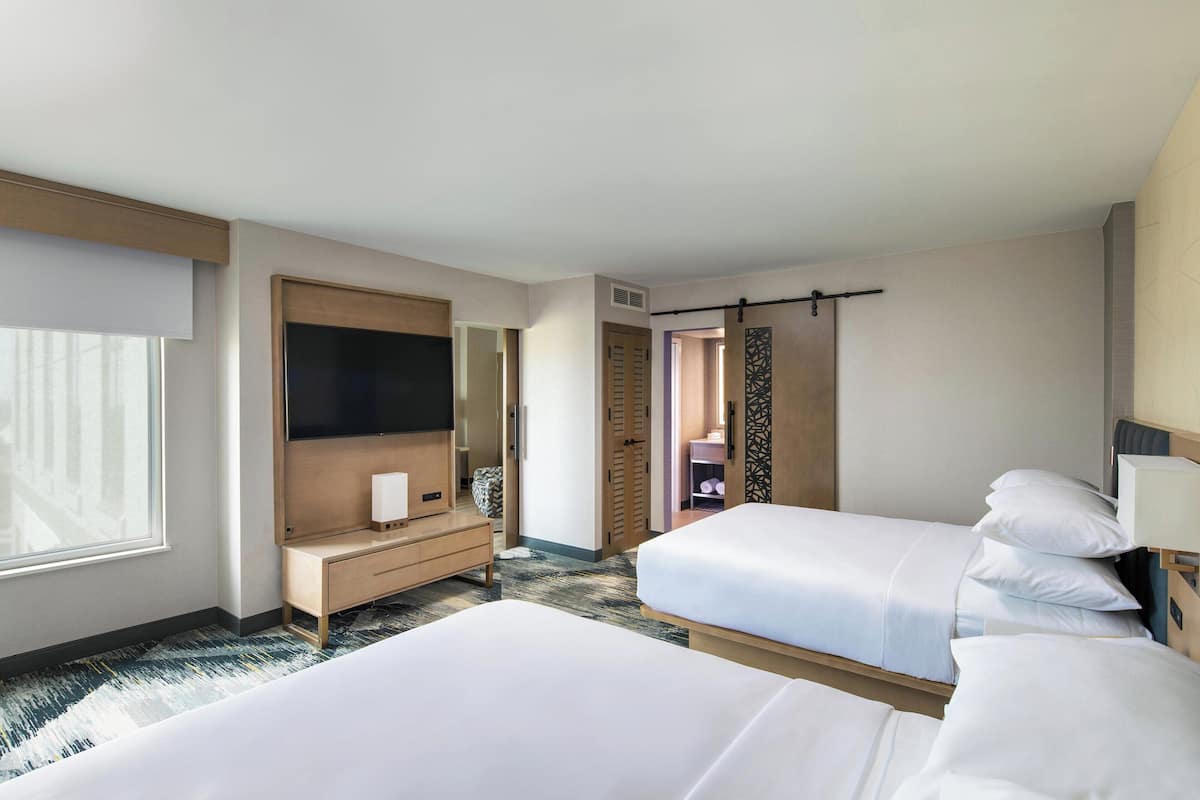 A hotel room with two beds, a TV, a desk, and a bathroom visible through an open door.