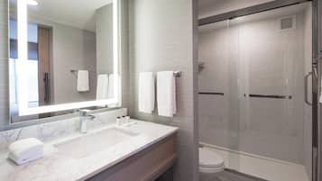 A modern bathroom with a large mirror, a marble sink, and a glass-enclosed shower.