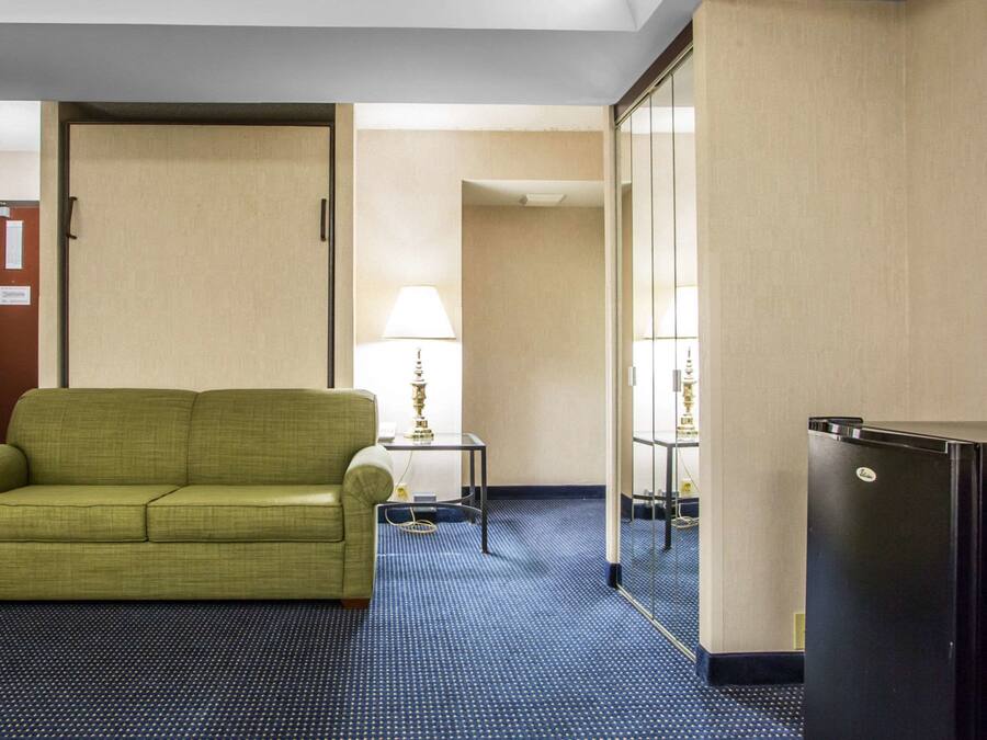Een hotelkamer met een groene bank, een tafeltje met een lamp en een koelkast.