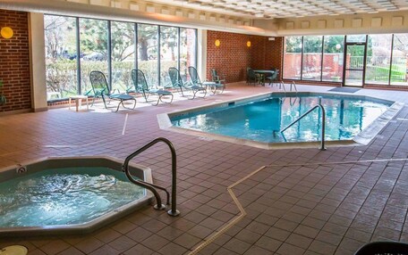 An indoor swimming pool with two separate sections, a brick wall, and a view of the outdoors through large windows.