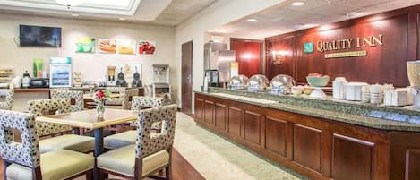 A hotel lobby with a buffet area, seating arrangements, and a reception desk.
