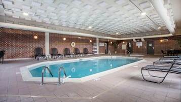 An indoor swimming pool with a brick wall, lounge chairs, and a ceiling with recessed lighting.