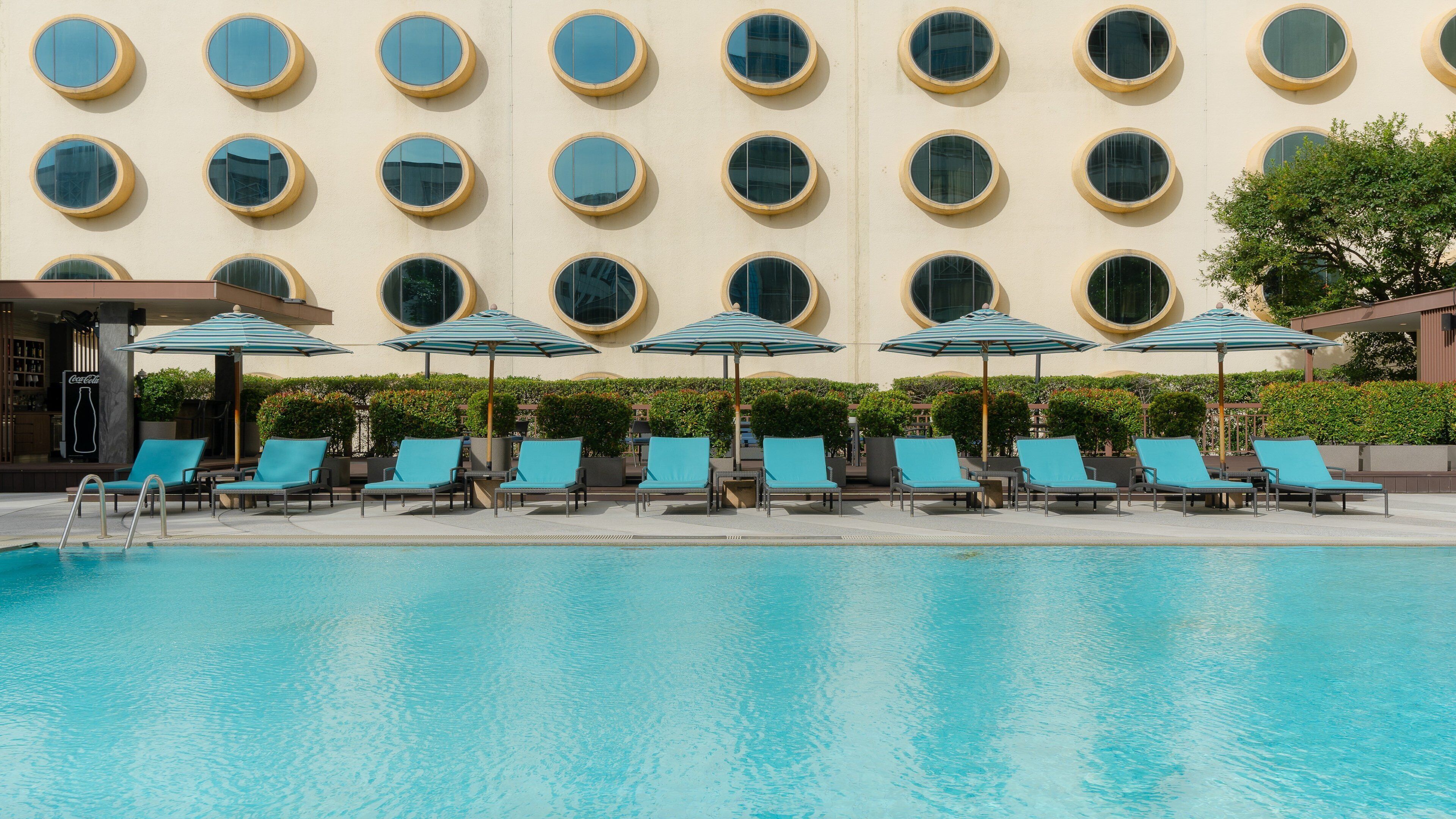 A swimming pool with lounge chairs and umbrellas, surrounded by a building with circular windows.