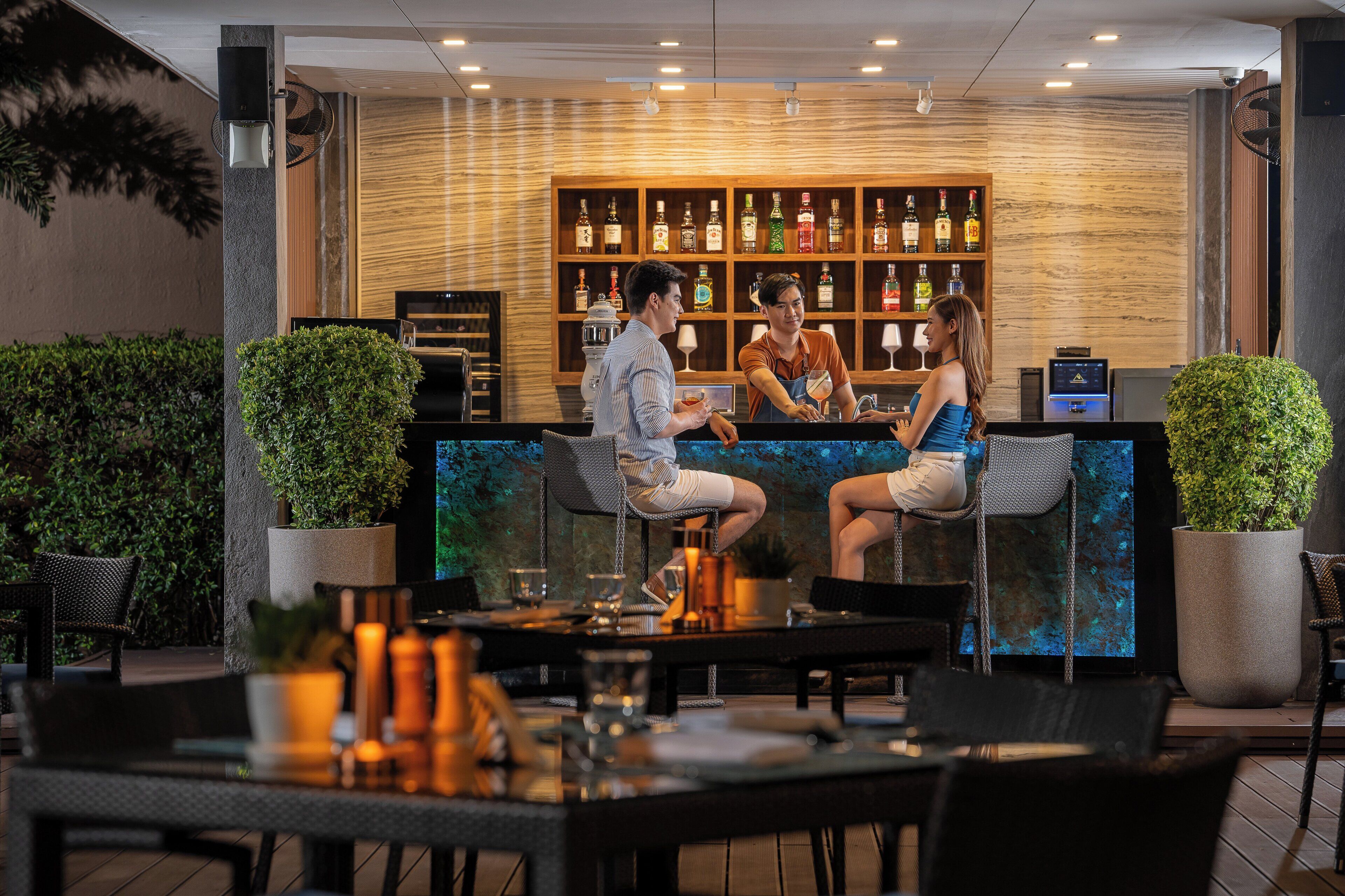 A bar area with a wooden shelf displaying various bottles, a counter, and seating for patrons.