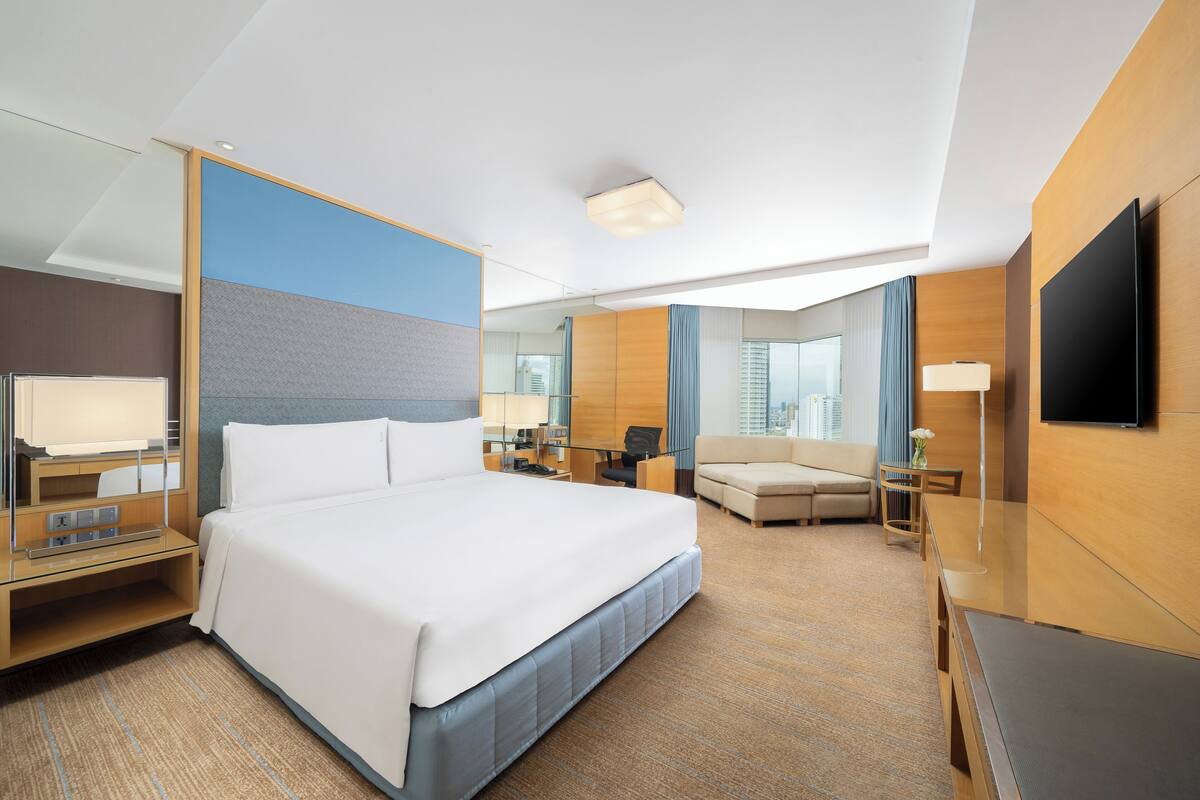 Habitación de hotel con una cama grande, un escritorio, una silla, televisión y vista a la ciudad.
