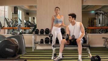 A gym with exercise equipment, a woman standing, and a man sitting on a bench.