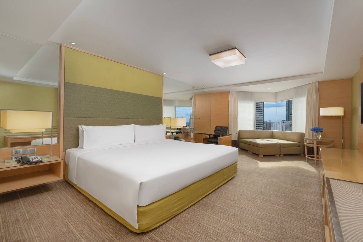 Una habitación de hotel con una cama grande, un escritorio con teléfono, una silla, un sofá, un televisor y una ventana con vista a la ciudad.
