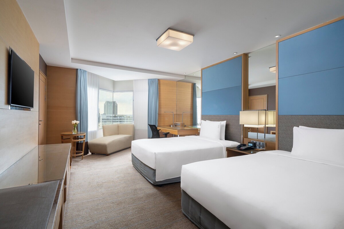 A hotel room with two beds, a desk, a chair, a TV, and a large mirror.