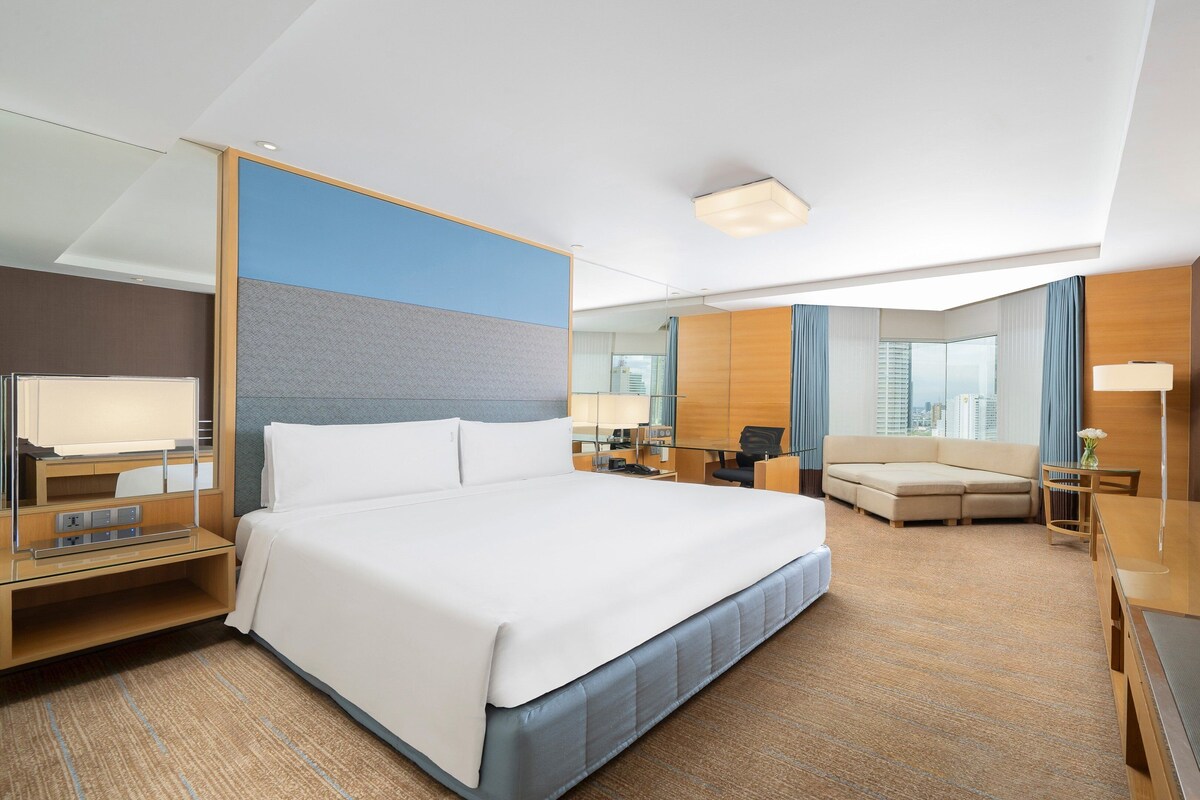 A modern hotel room with a large bed, a desk, a sofa, and a TV.