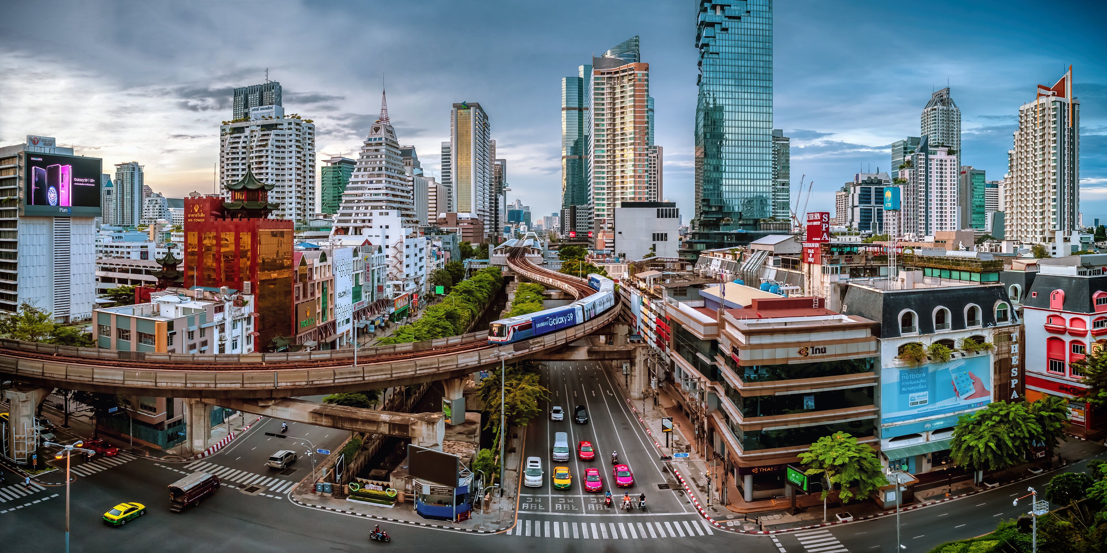 A cityscape with modern high-rise buildings, a train passing through an elevated track, and a busy street with vehicles.