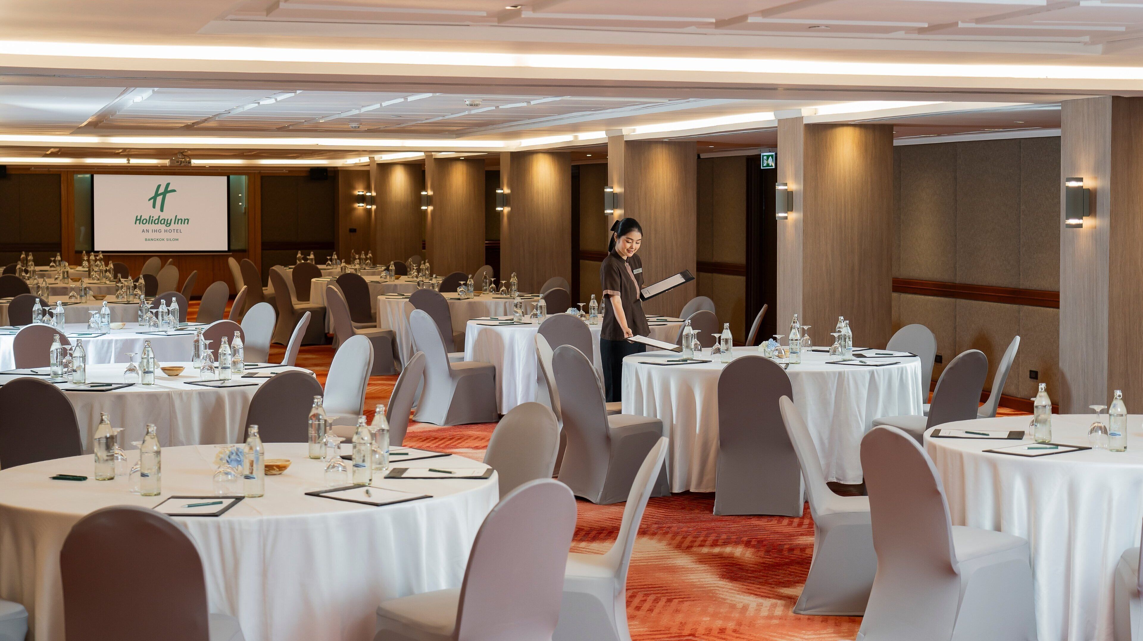 Een vergaderzaal van Holiday Inn met ronde tafels, stoelen en een projectiescherm op de achtergrond.