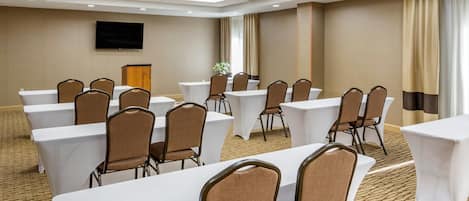 A conference room with multiple tables and chairs, a flat-screen TV on the wall, and a wooden podium.