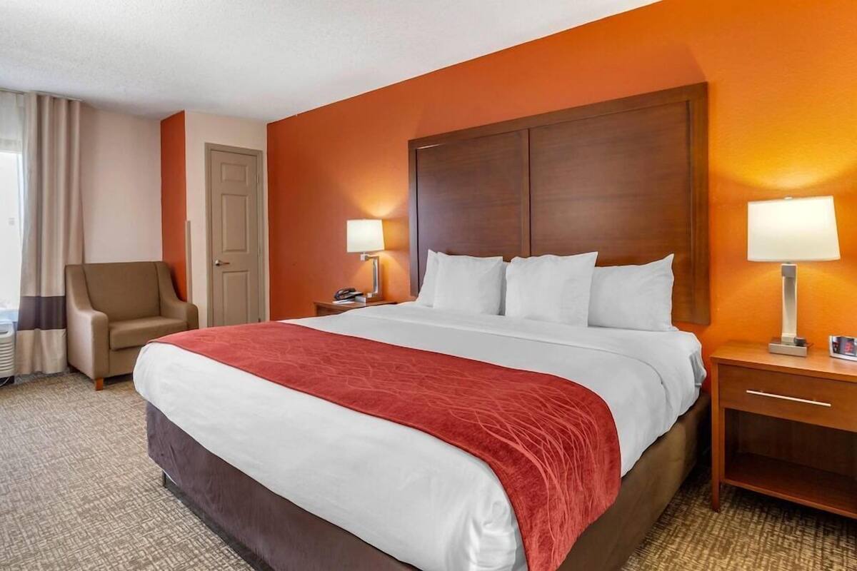 Une chambre d’hôtel avec un grand lit, deux lampes de chevet, une chaise, un bureau et une porte.