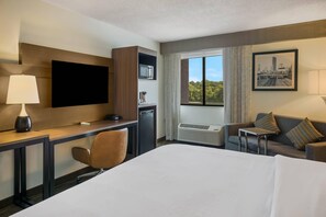 Habitación de hotel con cama, escritorio, silla, televisor, aire acondicionado y ventana con vista a la ciudad.