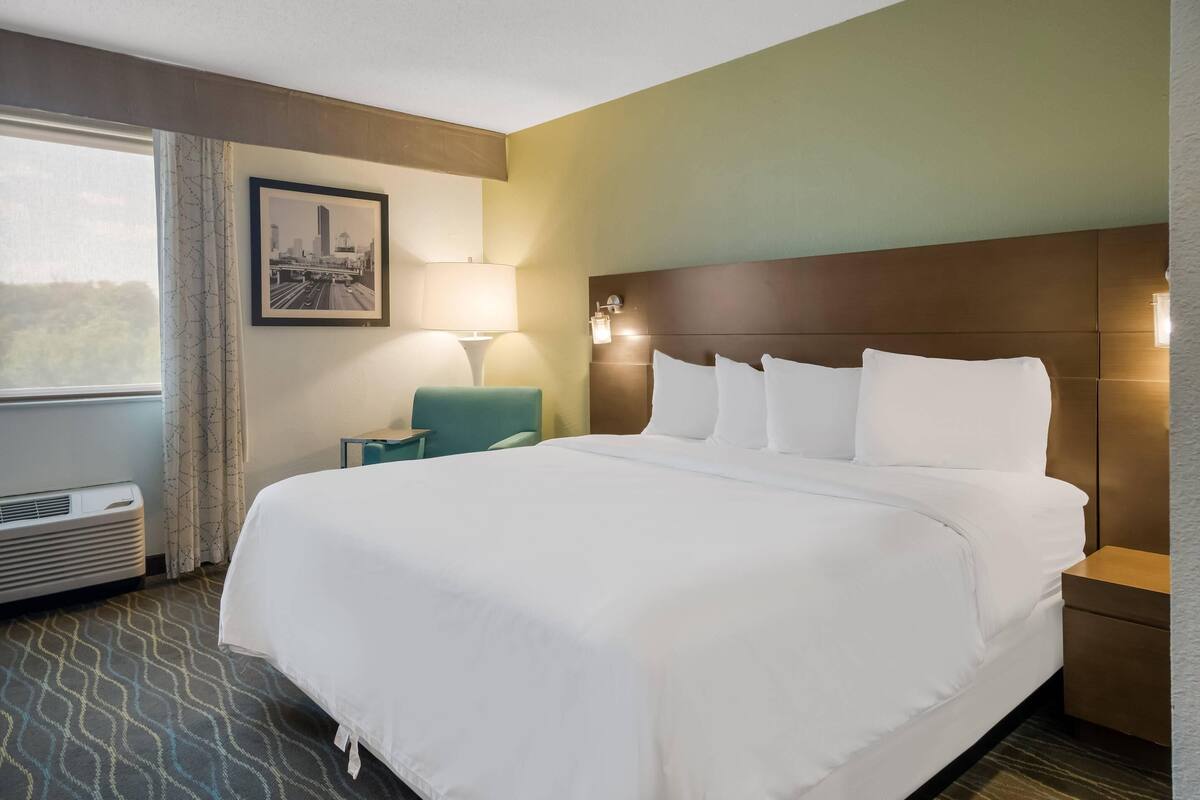A hotel room with a large bed, a desk, a chair, a window with curtains, and a wall-mounted picture.