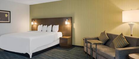 Una habitación de hotel con una cama grande, un sofá, una mesita y una lámpara.
