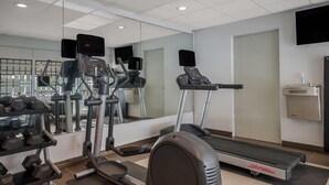 Una palestra con macchinari cardio, pesi e uno specchio lungo la parete.