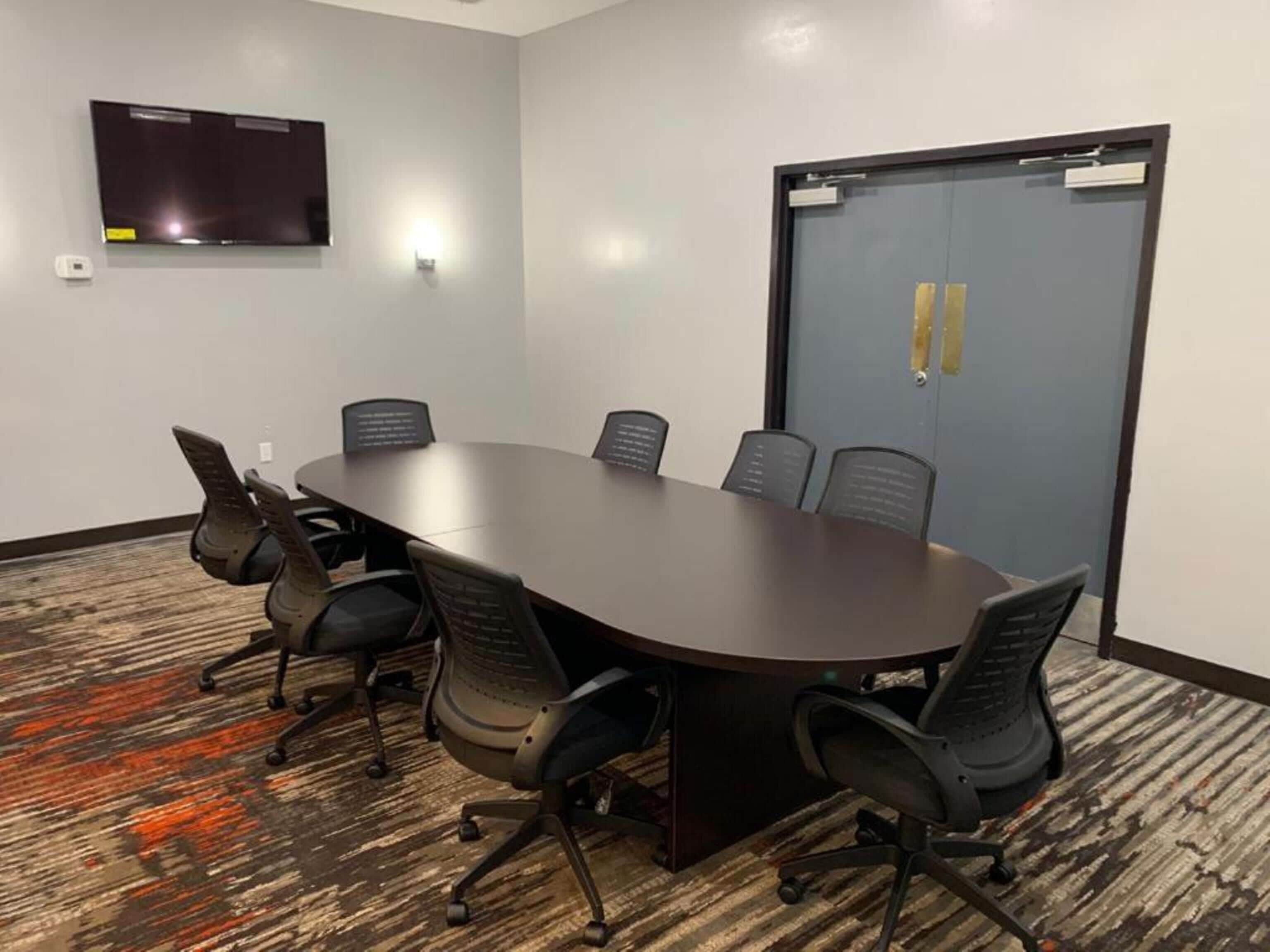 Una sala de conferencias con una mesa larga, seis sillas, un televisor de pantalla plana y una puerta con cerradura.