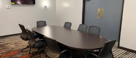 Una sala de conferencias con una mesa larga, seis sillas, un televisor de pantalla plana y una puerta con cerradura.