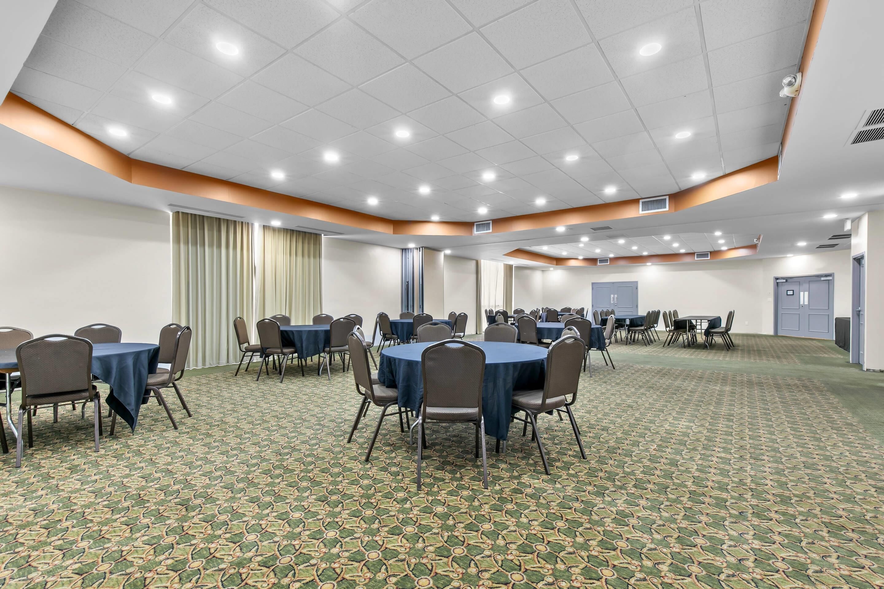 Une salle de conférence avec des tables rondes, des chaises et un tapis à motifs.