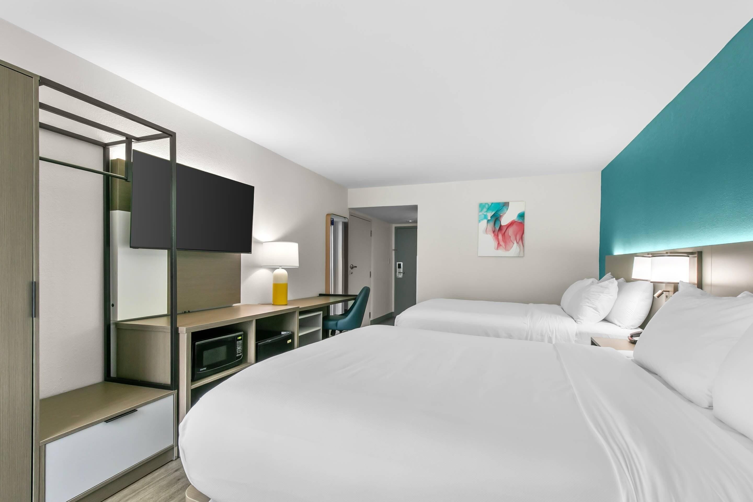 A hotel room with two beds, a desk with a lamp, a television, and a painting on the wall.