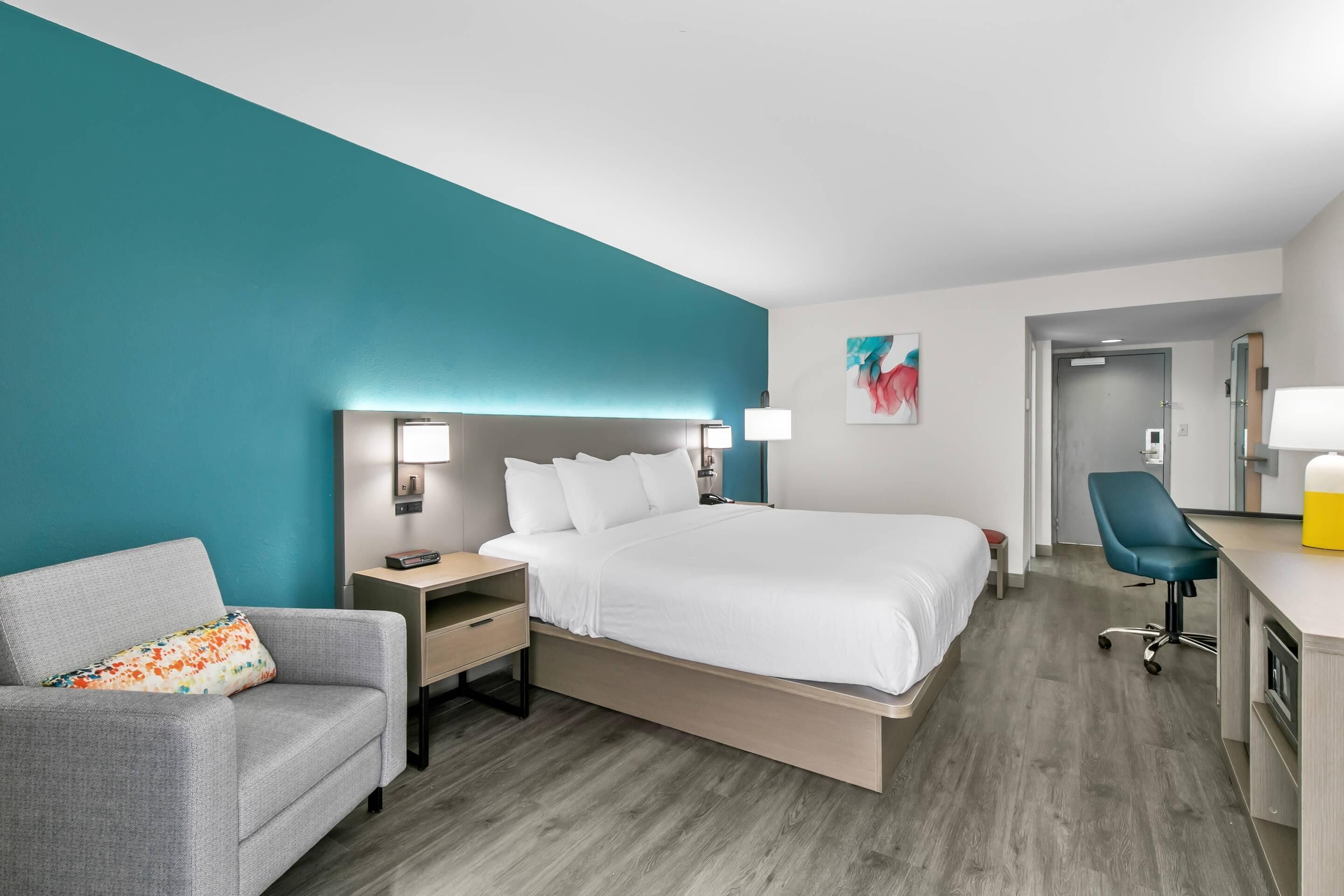 A hotel room with a bed, a desk, a chair, a sofa, and a nightstand.