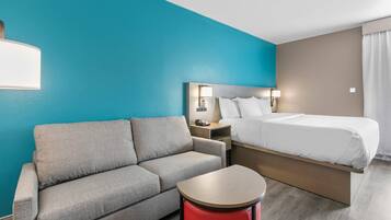 Quarto de hotel com cama, sofá, mesa pequena e mesa de cabeceira.