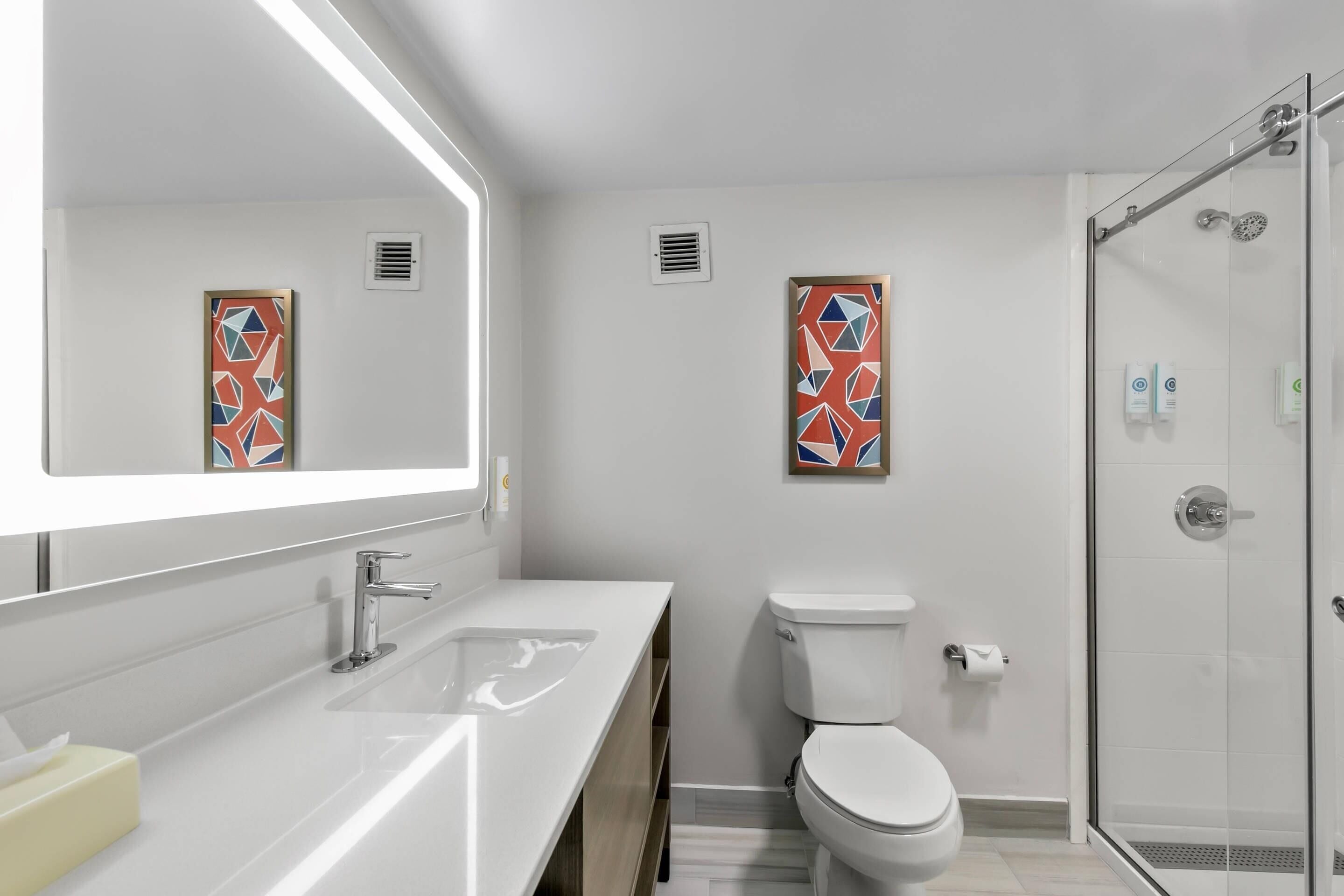 Ein modernes Badezimmer mit großem Spiegel, Waschbecken in Weiß, Toilette und Duschkabine.