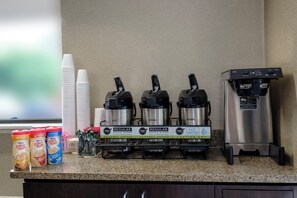 A coffee station with three Bunn coffee makers, a water dispenser, and various coffee pods and creamer options.