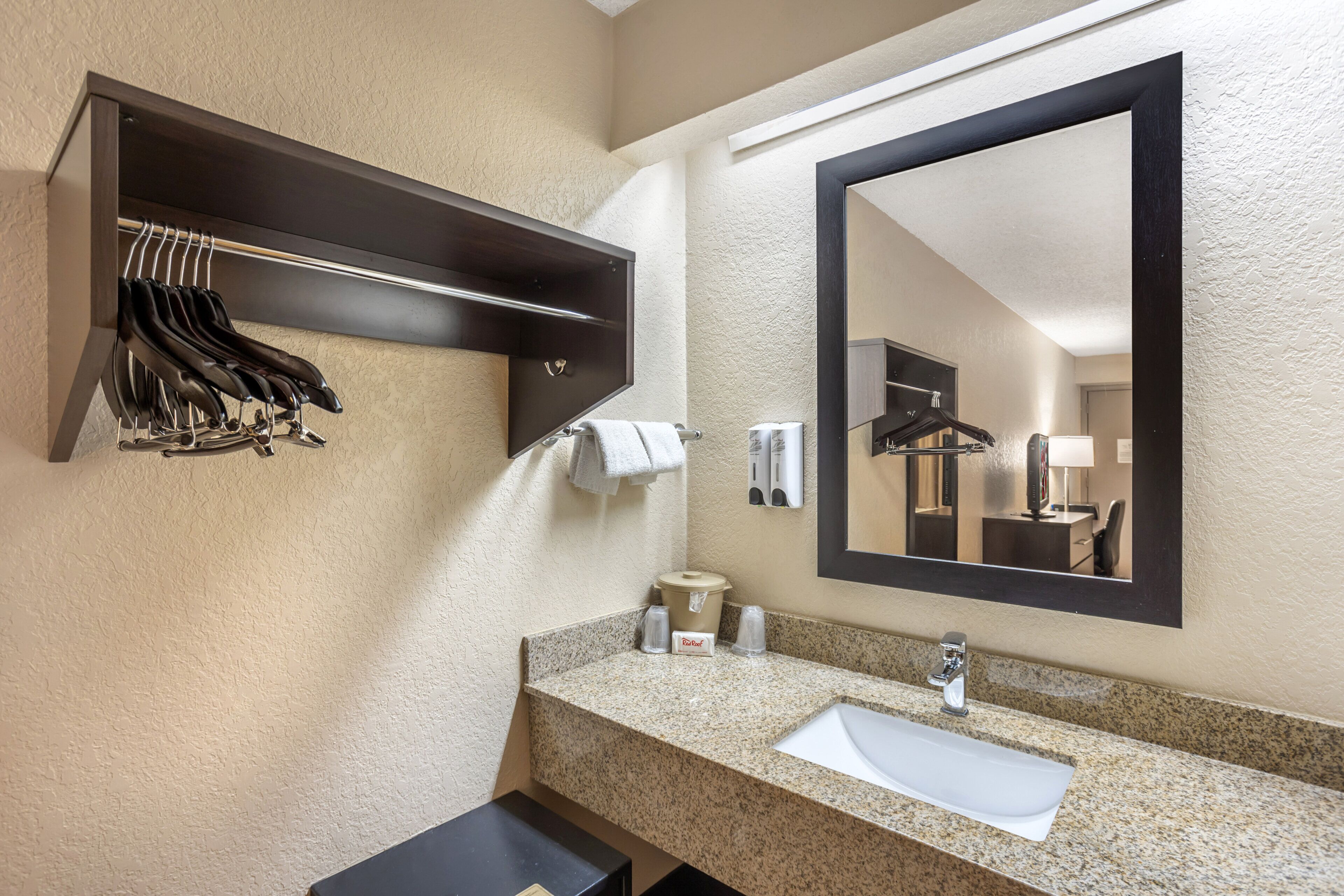 A hotel bathroom with a granite countertop sink, a mirror, a towel rack, and a small trash bin.