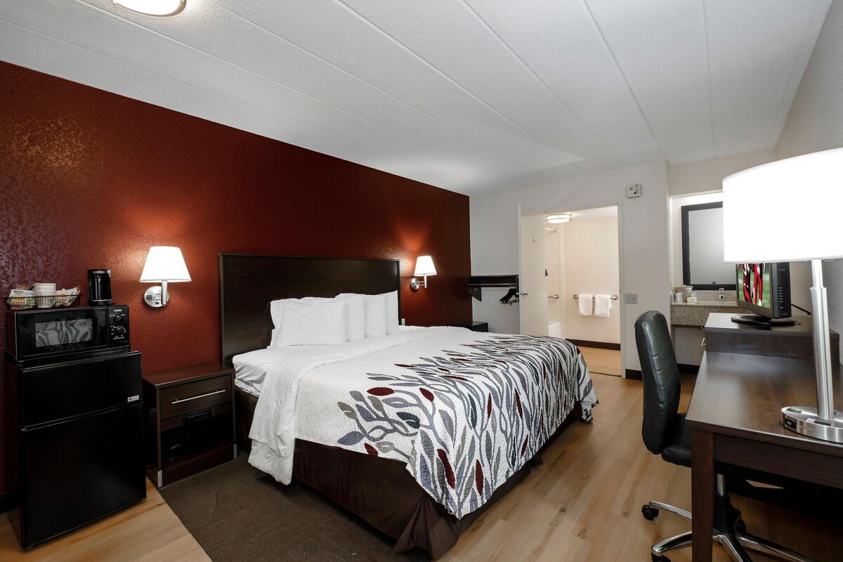 A hotel room with a bed, a desk, a chair, a microwave, a coffee maker, and a small kitchenette.
