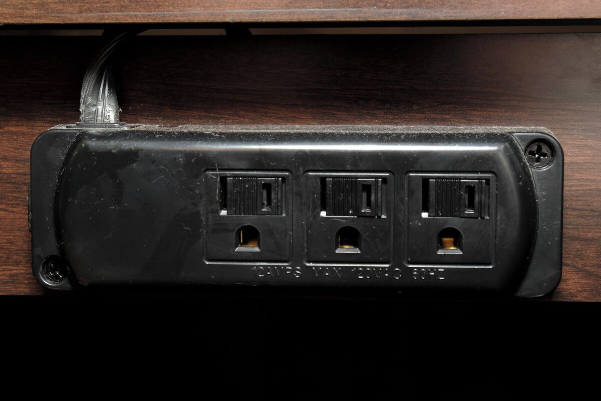 A black electrical outlet with three sockets, mounted on a wooden surface.