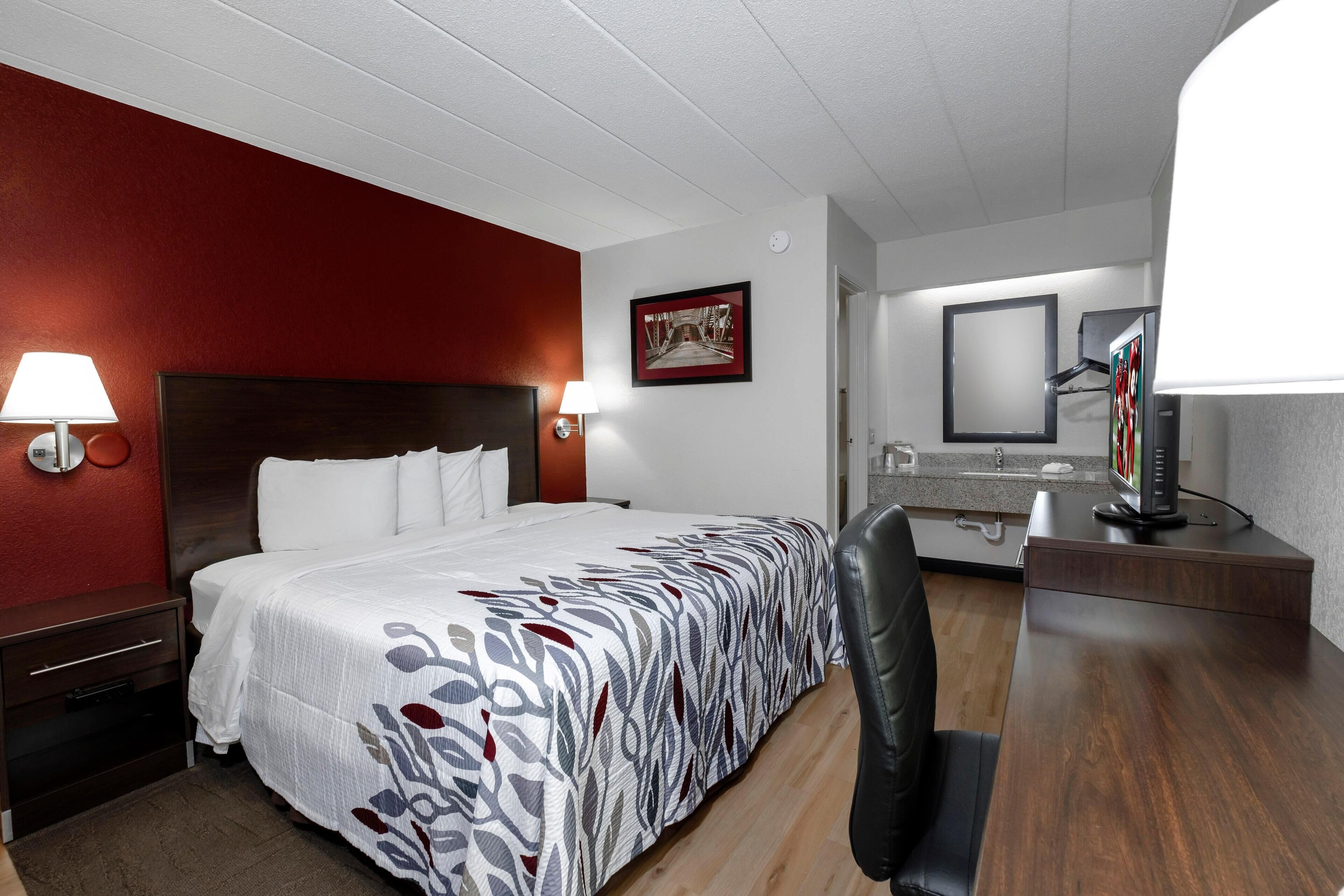 A hotel room with a bed, bedside lamps, a desk, a chair, a mirror, and a picture on the wall.