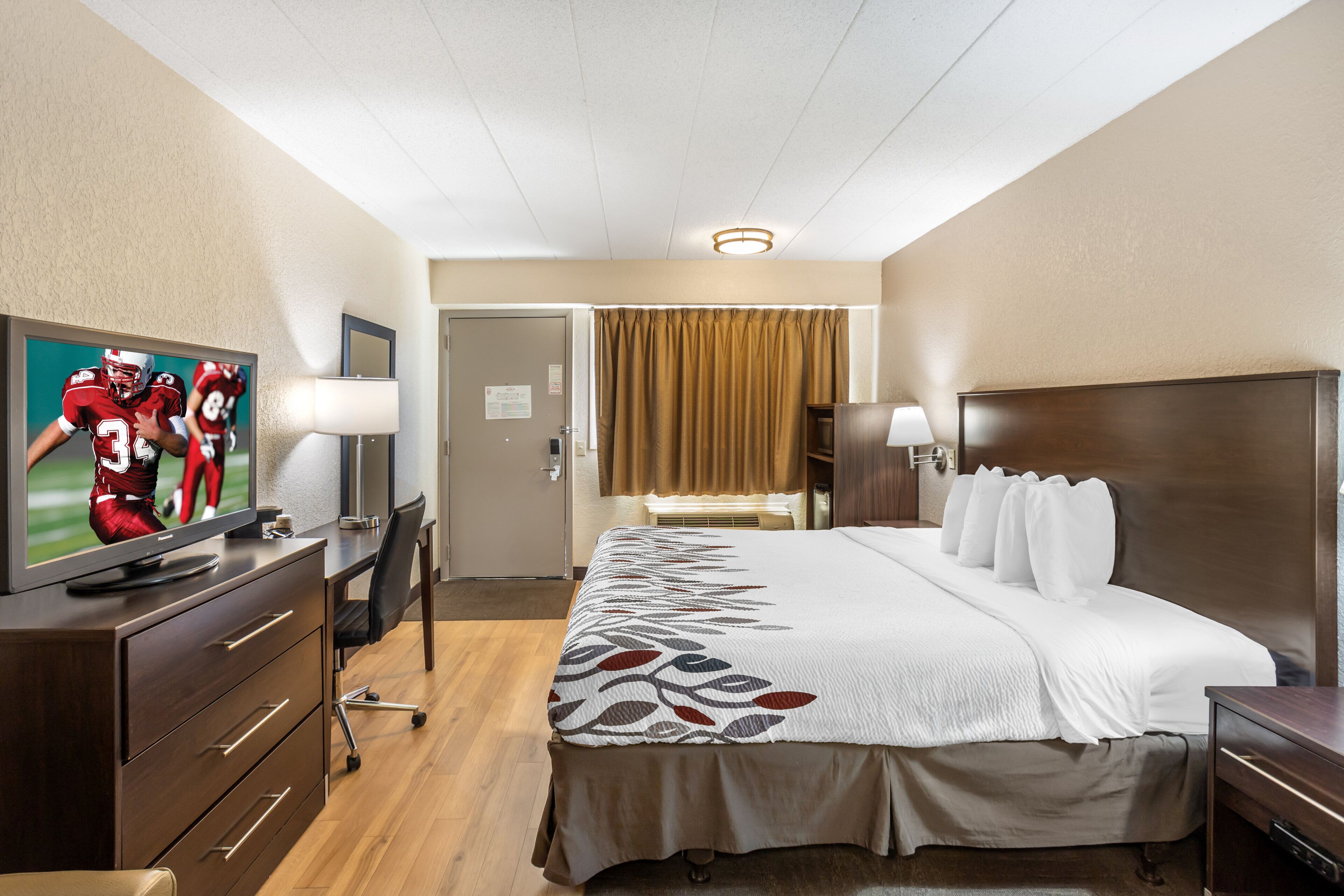 A hotel room with a bed, a desk, a television, and a door.