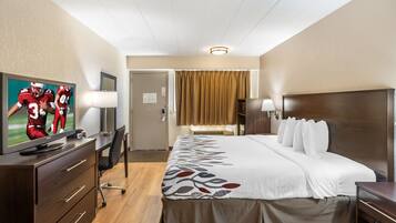 A hotel room with a bed, a desk, a television, and a door.