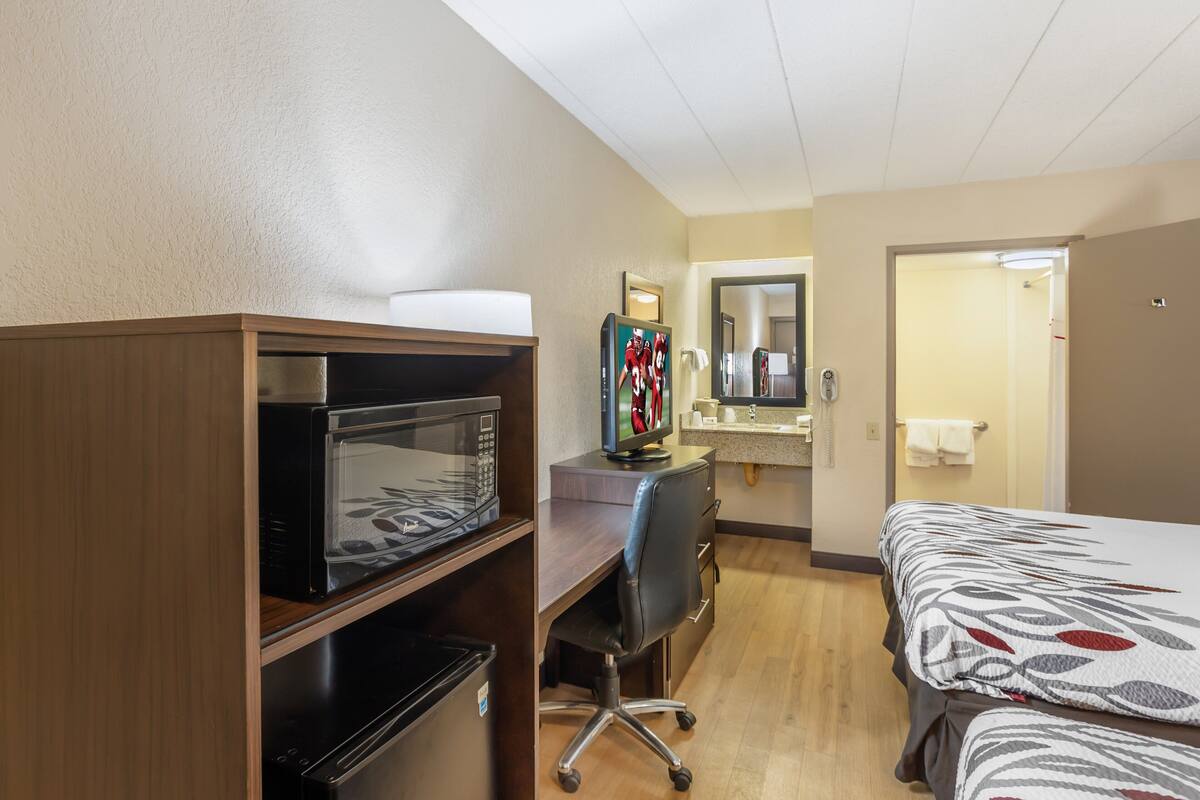 A hotel room with a bed, a desk with a computer, a microwave, and a small kitchenette.