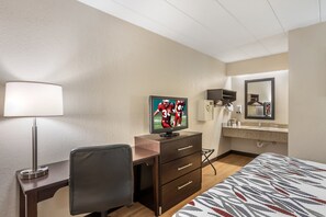 A hotel room with a bed, a desk with a chair, a television, a mirror, and a bathroom with a sink and mirror. - Red Roof Inn Danville, PA (Danville)