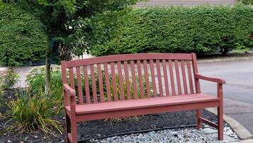 A red bench in a landscaped area with a hedge and plants in the background.