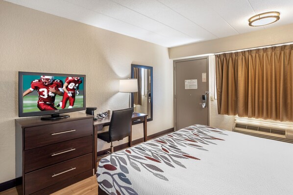 Una habitación de hotel con cama, escritorio, televisor y puerta.