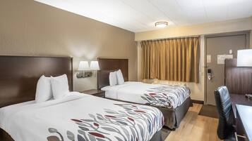 Ett hotellrum med två sängar, ett skrivbord, en stol, en lampa, en gardin och en dörr.