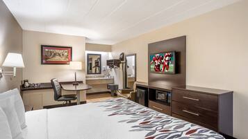 Quarto de hotel com cama, escrivaninha, cadeira, televisão, espelho e janela.