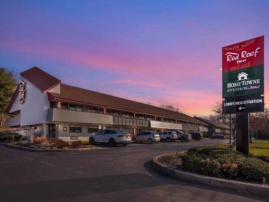 Un motel con un cartel de Red Roof Inn y Home Towne Studios. Hay coches aparcados en la parte delantera, y se ve un cartel para recepción.