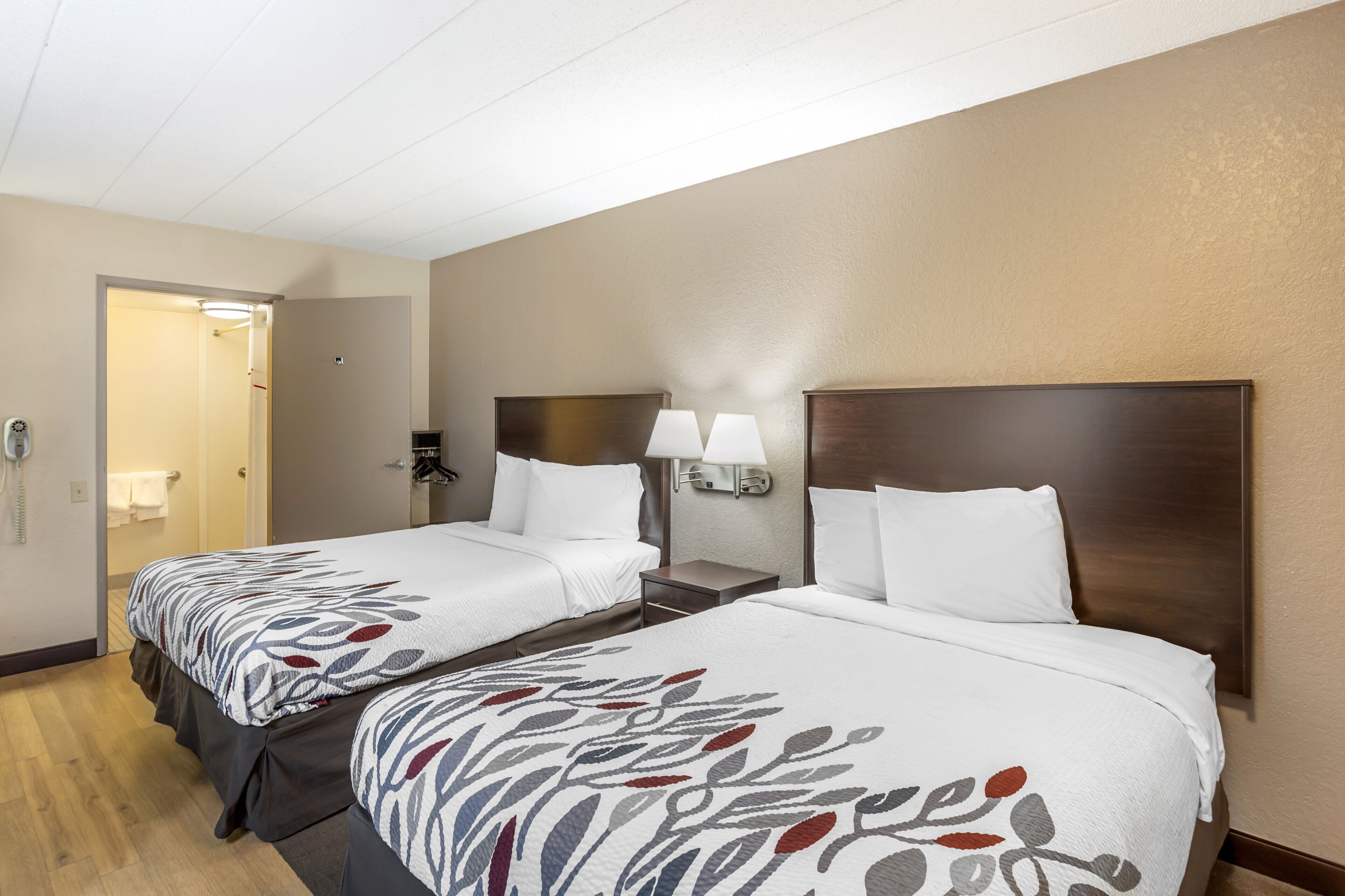 Una habitación de hotel con dos camas, cada una con una colcha estampada, lámparas de noche y cabeceros de madera.