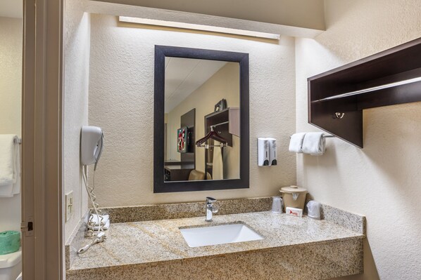 A hotel bathroom with a granite countertop sink, a mirror, a towel rack, and a hand dryer.