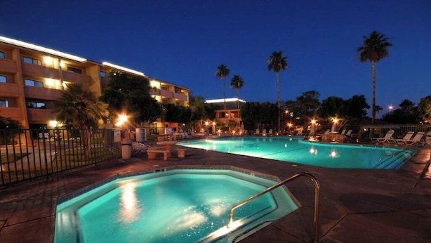 A hotel pool area with multiple pools, palm trees, and a building with illuminated windows.