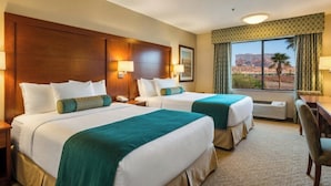 A hotel room with two beds, a desk, and a view of a desert landscape.