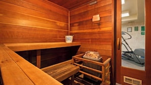 A sauna room with wooden walls, a bench, a small table with a basket, and a door leading to another room.