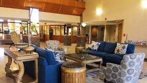 A lobby with a blue sofa set, patterned armchairs, a round wooden coffee table, and a decorative side table.