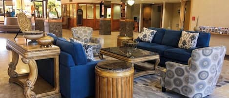 Um hall de entrada com um sofá azul, poltronas estampadas, uma mesa de centro redonda de madeira e uma mesinha lateral decorativa.